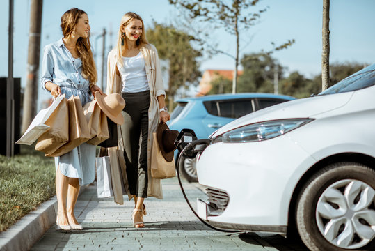 Women walking with shopping bags to their electric car on the shopping mall parking otudoors