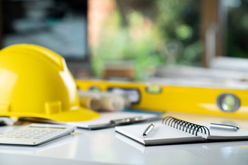 Contractor concept. Yellow hardhat, libella and plans on the white table.