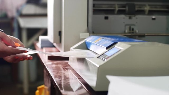 Putting and insert laminating film with paper in laminator. Woman laminating paper in laminating machine in typography hands closeup. Hot and cold lamination machine. Publishing business and industry.