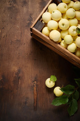 Freshly harvested small apples in box with leaves on wooden background