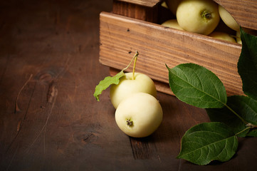 Freshly harvested small apples in box with leaves on wooden background