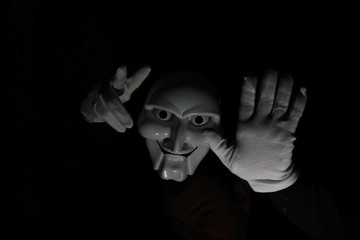 White scary mask on a black background with whites hand.