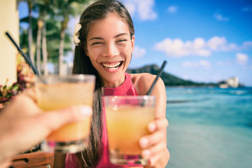 Cocktail toast couple going out on beach restaurant cheering with rum mai tai drinks on Waikiki, Honolulu, Hawaii travel. Happy Asian woman holding glass of alcohol toasting with man.