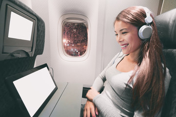 Passenger in airplane using tablet computer. Woman in plane cabin using smart device listening to music on headphones. Banner panorama travel people lifestyle.