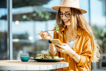 Stylish young woman eating healthy salad on a restaurant terrace, feeling happy on a summer day - Powered by Adobe