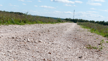 the road is paved with gravel. travelling by car. hinterland. in the background, a cell tower. white large crushed stone. road to village. beautiful weather. travel in summer. endless meadows and fiel