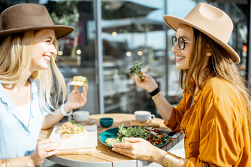 Two female best friends eating healthy food while sitting together on a restaurant terrace on a summer day