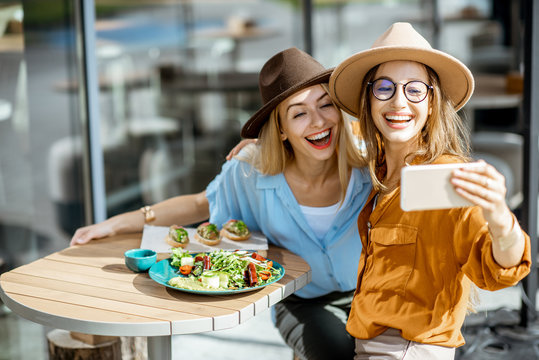 Two female best friends making selfie photo while sitting together on a restaurant terrace and eating healthy food