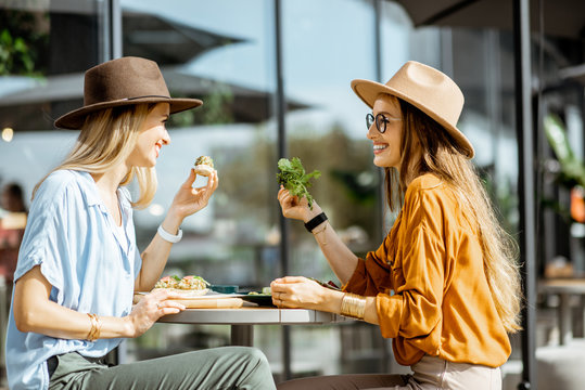 Two female best friends eating healthy food while sitting together on a restaurant terrace on a summer day