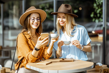 Two female best friends spending time together on the cafe terrace, feeling happy standing with...
