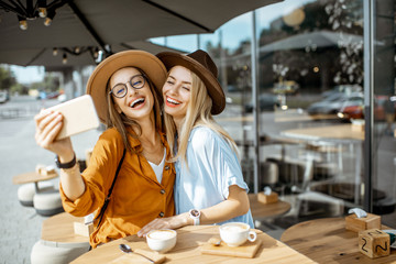 Fototapeta Two female best friends making selfie portrait while spending time together on the cafe terrace during a summer day obraz