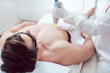 Cosmetologist using laser to remove chest hair of man