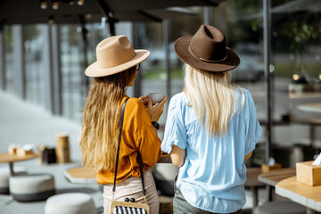 Two girlfriends standing together at the cafe terrace, rear view