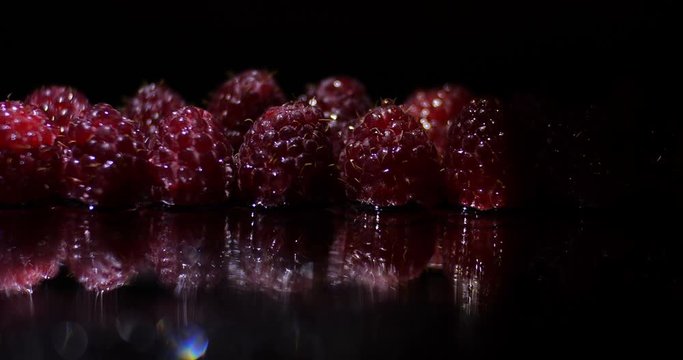 
Close up macro studio light movement  along a row of fresh raspberries in water droplets with bokeh on a black background with reflection, dramatic light changing . 4K
