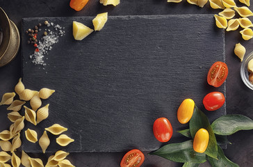 Pasta shells on black stone. Tomatoes and bay leaves with allspice and sea salt.