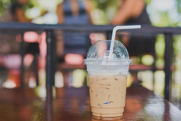 Side view Ice coffee (cappuccino, latte, mocha) in plastic cup with water drop on wooden table with blurry cafe background with copy space for your text. Vintage tone