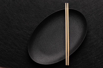 Empty oval black plate with chopsticks on dark background. Japanese food style. Top view with copy space
