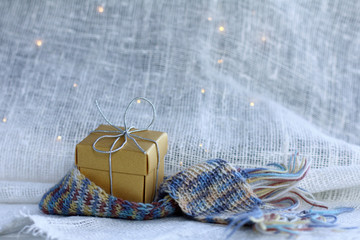 holiday gift in a knitted scarf on a background of light fabric with garland lights. Christmas surprise with warm feelings