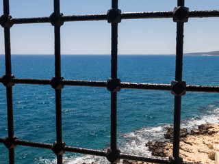 A view of sea and coastline through the metal bars of ancient building window