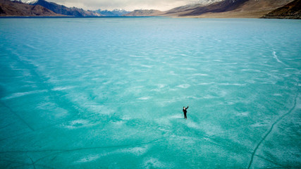 Man walking on Surface of Frozen Lake from drone aerial view at Pangong Lake or Pangong Tso, Tso moriri, Nubra, India. Abstract concept of Cold winter, peaceful and freedom.