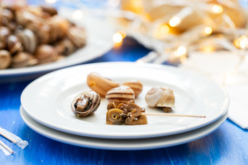 boiled snails on white plate on blue wooden background