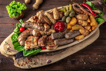 Assorted meat. A large beautiful wooden plateau with juicy pieces of pork, beef, chicken, meat.  Grilled sausages, bones, ribs, fillets, barbecue with appetizer of pickles and potatoes. 