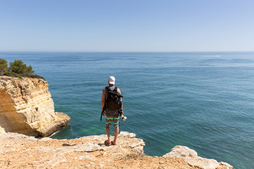 Obraz premium Mann mit Kamera steht auf den Klippen am Meer