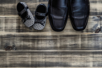daddy's black business shoes and black and white kids sneakers side by side on grunge rusty wood, concept of family, single parent and father's day, Top view flat lay with copy space.