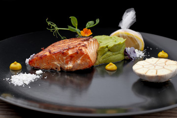 Piece of the fried salmon on a black dish with a lemon. steak. Filet