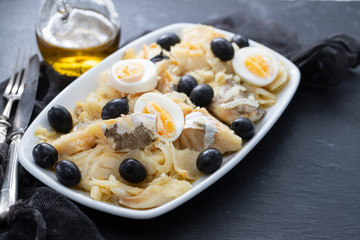 cod fish with onion, olives, eggs and olive oil on dish on ceramic background