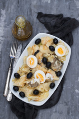 cod fish with onion, olives, eggs and olive oil on dish on ceramic background