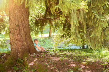 Cute little boy sitting and dreaming under a big tree