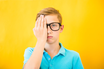 Sad teen boy looks with one eye while covering his other eye with his hand. Medicine, ophthalmology and glasses selection concept