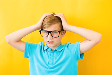 Frustrated boy holding his head on a yellow background. Study, difficulties and problems concept