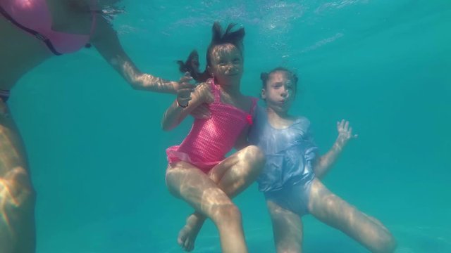 Two cute little girls swim and have fun under the water in the pool on vacation. They pose for the camera, smile and wave their hands. Close up. Concept video. 4K.