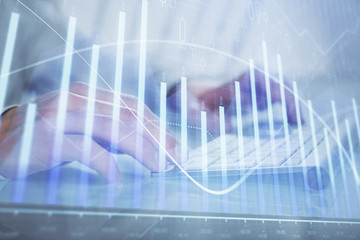 Double exposure of graph with man typing on computer in office on background. Concept of hard work.