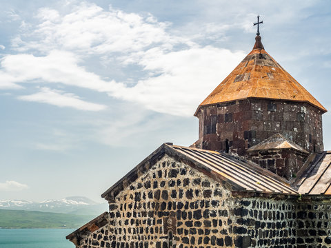 Top part of Surp Karapet church in ancient Sevanavank monastery, with lake Sevan and snowy mountains seen in the distance.