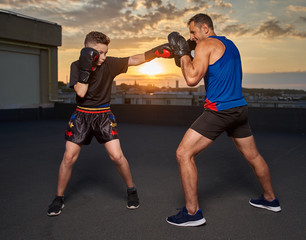 Young fighter hitting pads with trainer at sunset