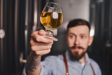 Bartender in the apron checks beer quality holding it in front of himself.