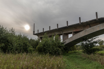 an unfinished bridge stands on the river in the meadow