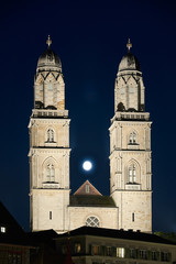Fototapeta premium Zürich Grossmünster, Vollmond zwischen den beleuchteten Zwillingstürmen, dunkler Nachthimmel