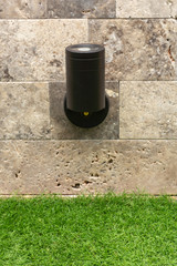 Street lamp backlight from the bottom up on a stone wall against a background of green grass.