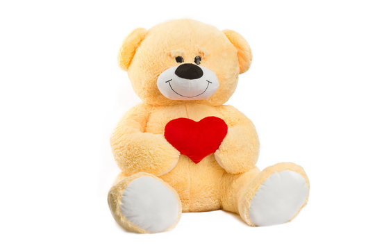 Image of golden toy teddy bear holding red heart and sitting at isolated white background.