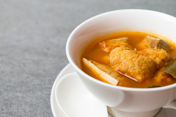 Spicy soup or orange curry of Thai with fish in white bowl and spoon on concrete table.