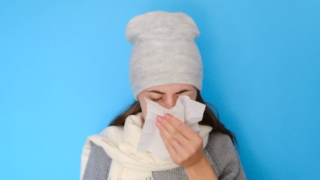 Ill allergic woman blowing running nose got flu caught cold sneezing in tissue isolated on blue blank studio background, sick female student girl having hay fever allergy symptoms holding handkerchief
