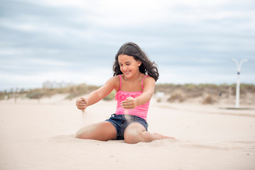 Fototapeta na wymiar Pretty girl playing with the sand on the beach