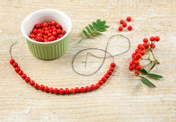 Making protective rowan berry charm necklace, it is believed that rowan tree berries have magical properties. Old folklore concept. Light natural wooden background.