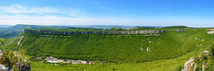 Fototapeta na wymiar View of the mountain covered with a green carpet of trees and grass, on a bright sunny day, with clouds in the sky. Spring view of the Crimean mountains.