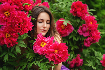 Naklejka premium Beautiful Romantic Girl is sitting near pink peonies.Gorgeous young model dreaming with close eyes in spring garden.