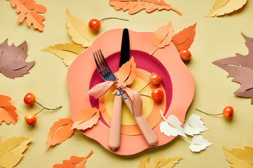 Table setup for Autumn celebration. Bright plastic plate on yellow paper with paper Autumn leaves